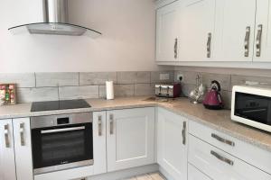 a kitchen with white cabinets and a stove and microwave at BROOK COTTAGE in Whitstable