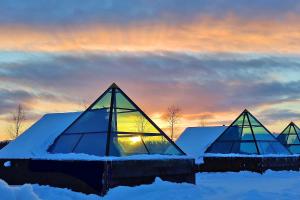 Köngäs的住宿－Hotel Taivaanvalkeat，一组玻璃金字塔在雪中,伴着日落