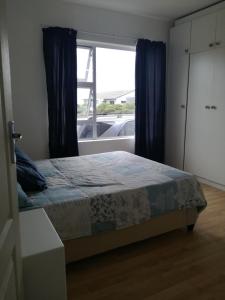 um quarto com uma cama com cortinas azuis e uma janela em Gansbaai Self-Catering Apartment em Gansbaai