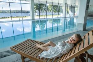 a little girl laying on a bench next to a swimming pool at Notera Hotel SPA in Charzykowy