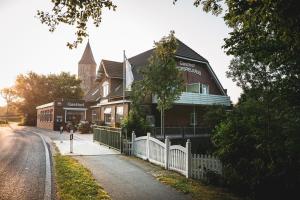 a building with a white fence and a church at Kirchspielkrug Landhotel & Restaurant in Westerhever