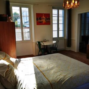 a bedroom with a bed and a table and windows at Le Bonheur- Suite Cognac in Hiersac