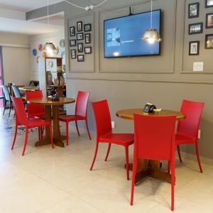 a restaurant with red chairs and tables and a tv on the wall at Hotel Maraja in Uberlândia