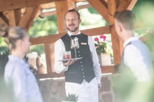 Um homem de colete e gravata borboleta a segurar um prato de comida. em Rainell Dolomites Retreat em Ortisei