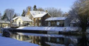 a house is covered in snow next to a river at Riverside Cottage in Hilgay