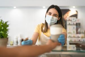 uma mulher usando uma máscara facial e luvas segurando um copo em Campanile Amiens - Glisy em Glisy