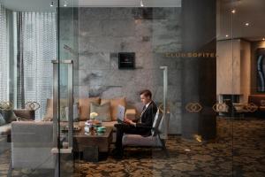a man sitting in a chair with a laptop in a lobby at Sofitel Wellington in Wellington