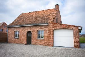 una casa in mattoni rossi con un garage bianco di Huis van de Koekuit a Moorslede