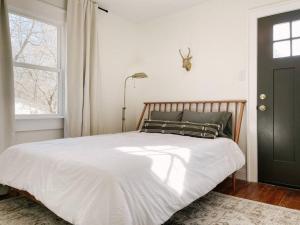 a bedroom with a bed with white sheets and a window at Revived Schoolhouse near Downtown and UT Campus in Knoxville
