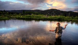 un hombre está de pie en un río sosteniendo un pez en Relax in The Rockies Located on Lake Estes, Jacuzzi and Indoor Outdoor Fireplace, en Estes Park