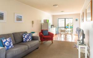 sala de estar con sofá gris y silla roja en Snells Beach Motel, en Snells Beach