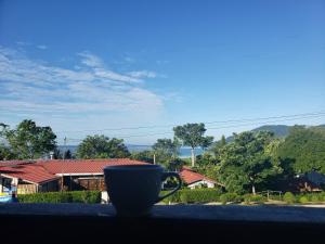una taza de café sentada en el alféizar de una ventana con una casa en Hotel y Restaurante Las Gardenias, en El Remate