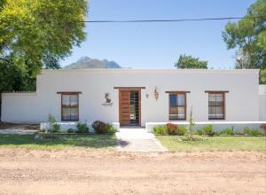 a white house with a door and windows at De Kale Kat in Greyton