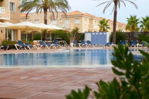 a swimming pool with chairs and umbrellas and palm trees at Apartamentos Las Dunas-B in Riumar
