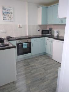 a kitchen with white cabinets and a wooden floor at Flat by the sea in Paignton