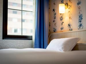 a bed with a white pillow and a window at Hotel Eclair Hakata in Fukuoka