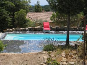 a red chair sitting next to a swimming pool at Les Romarins in Aigne