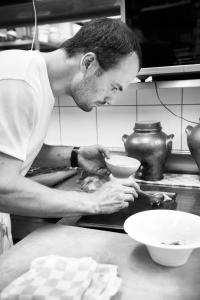 Un uomo in cucina che prepara una ciotola su un bancone di Hotel La Ferronniere a Bouillon
