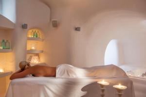 Una donna sdraiata su un letto in una stanza con le candele di On The Rocks - Small Luxury Hotels of the World a Imerovigli