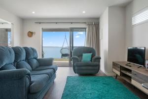 ein Wohnzimmer mit einem blauen Sofa und einem TV in der Unterkunft Soleil on Omana - Omana Beach Holiday Home in Maraetai