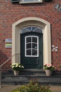 een groene deur op een bakstenen gebouw met twee potplanten bij Göcke's Haus und Garten in Wettringen