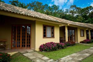 una pequeña casa amarilla con flores en el patio en Casas Di Monte Ecopousada, en Morretes