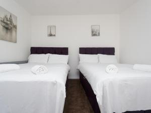 two twin beds in a room with white sheets at Eastpark Residence in Leeds