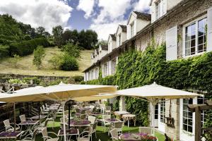 an outdoor patio with tables and chairs and umbrellas at Logis Hôtel Le Beaulieu in Beaulieu-sur-Dordogne