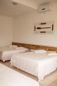 a room with three beds with white sheets at Pousada Pescador in Ubatuba