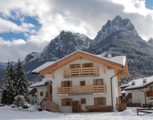 une maison dans la neige avec des montagnes en arrière-plan dans l'établissement Ciasa Rasom, à Pozza di Fassa