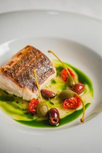a plate of food with a piece of fish with grapes and olives at Borgobianco Resort & Spa Polignano - MGallery Collection in Polignano a Mare