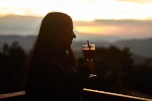 a woman holding a glass of wine with the sunset in the background at Coffee & Adventure Hotel by La Palma y El Tucan in Zipacón