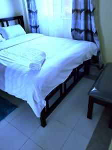 a bedroom with a bed with a white blanket and a bench at Standard Gardens 1-2-3 bedrooms Apartment Kisumu in Kisumu