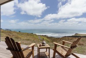 2 Stühle und ein Tisch auf einer Terrasse mit Meerblick in der Unterkunft Castaways Resort in Waiuku