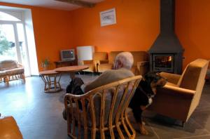 Ein Mann sitzt auf einem Stuhl mit einem Hund im Wohnzimmer. in der Unterkunft Ecurie du Warlet in Ambly