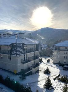 a building in the snow with the sun behind it at Apartament Prestige Szklarska Poręba in Szklarska Poręba