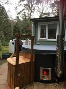 Woodland Cabin With private Wood-Fired Hot-Tub في فارنهام: حوض استحمام ساخن في الفناء الخلفي مع موقد