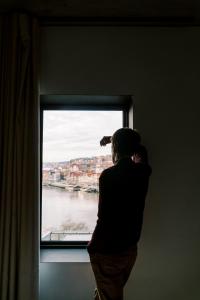 Un uomo che guarda fuori da una finestra verso l'acqua di Oh! Porto Apartments a Vila Nova de Gaia