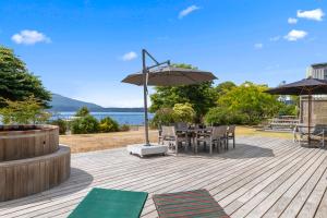 Lake Tarawera的住宿－Winstone Cottage - Waterfront Lake Tarawera Home，木甲板配有桌子和遮阳伞