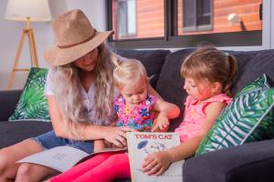 a woman and two little girls sitting on a couch reading a book at BIG4 Whitsundays Tropical Eco Resort in Airlie Beach