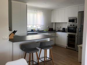 a kitchen with white cabinets and a counter with two bar stools at Ático a 200m del mar. in Jávea