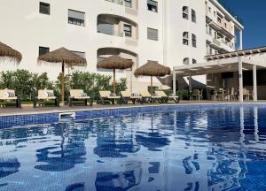 een zwembad met stoelen en parasols naast een gebouw bij Agua Hotels Alvor Jardim in Alvor