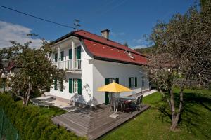 ein weißes Haus mit einer Terrasse und einem gelben Regenschirm in der Unterkunft Ferienhaus Kleine Gartenvilla in Pörtschach am Wörthersee