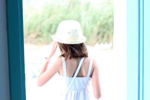 a young woman wearing a white hat looking out a window at Ploes Seaside Houses in Plaka