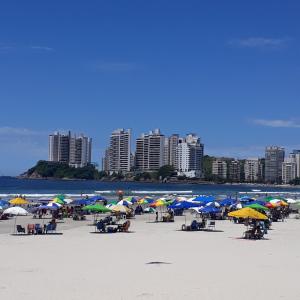 una spiaggia con un mucchio di ombrelloni e persone sopra di Kitnet em Guarujá - Pitangueiras (sem garagem) a Guarujá