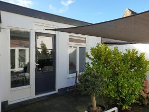 a white house with a black door and a tree at Little Lodge Noordwijk aan Zee in Noordwijk