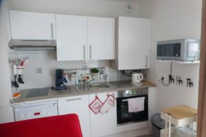 a small kitchen with white cabinets and a red chair at Studio Cosy neuf proximité du Golf et de la Digue in Wimereux