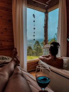 a woman laying in a bath tub with a glass of wine at Cabana Refúgio - Pousada Colina dos Ventos in Urubici