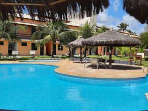a pool with chairs and umbrellas next to a building at Village Acapulco - Itacimirim/BA in Itacimirim