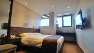 a bedroom with a large bed and two windows at Grandmillions Hotel Seogwipo in Seogwipo